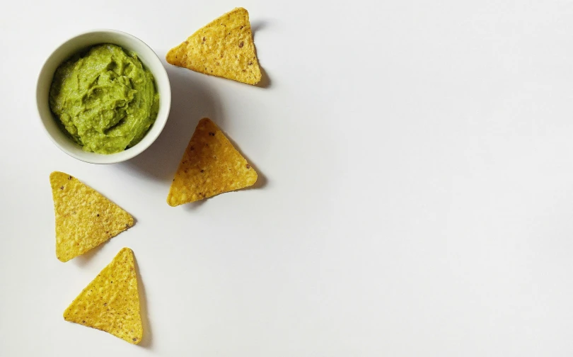 several small tortilla chips with guacamole in a small bowl