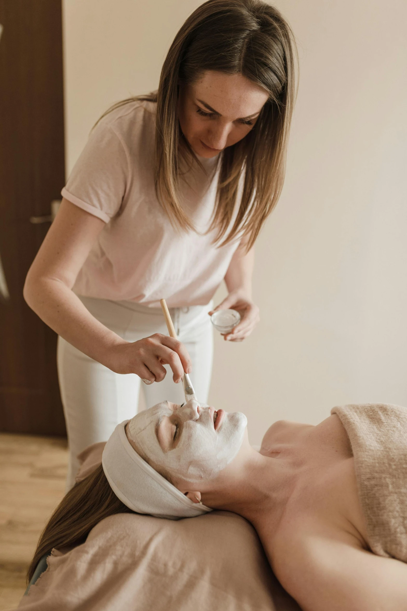 a woman standing over a mans head getting a facial mask