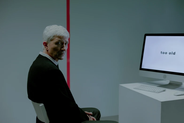 a man with white hair sitting in front of a desktop computer