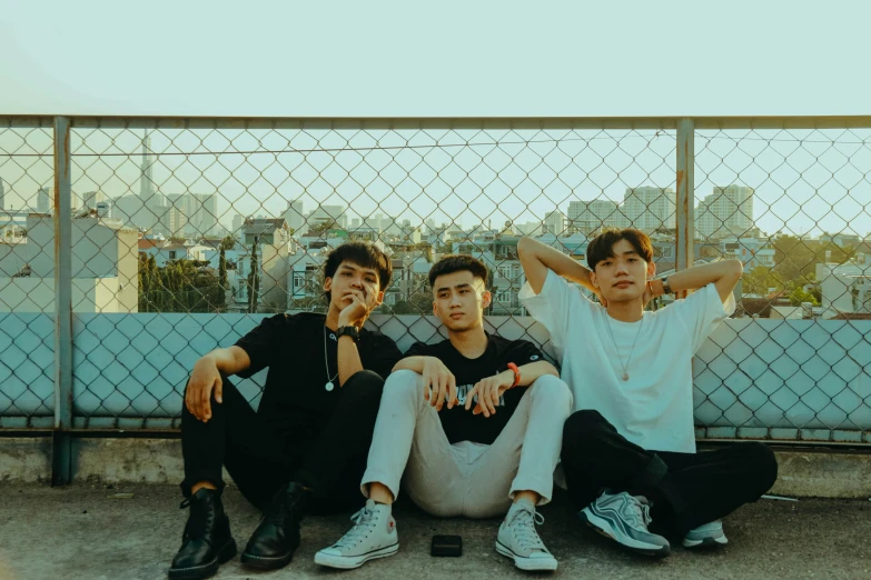 three boys pose together for the camera as they sit by a fence