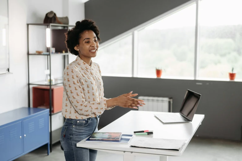 a woman stands near a white table with a laptop