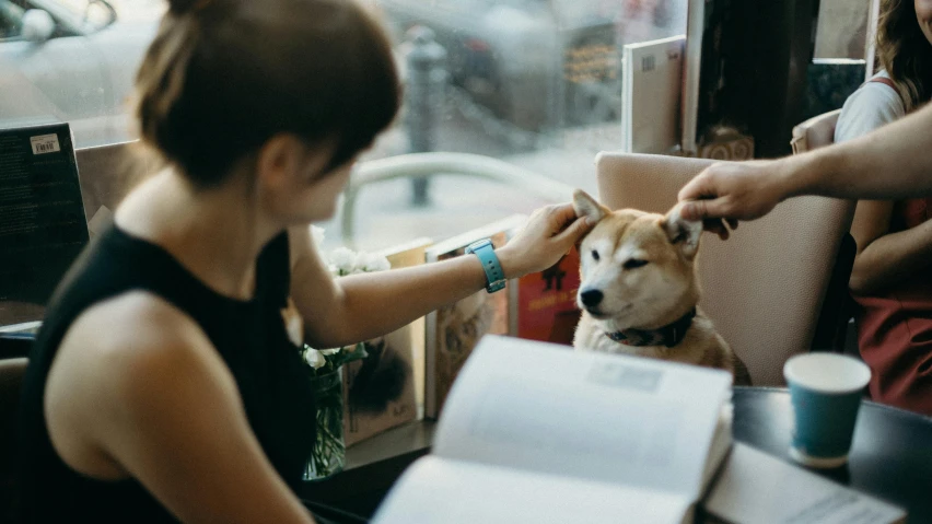 a woman is sitting at a table petting a dog