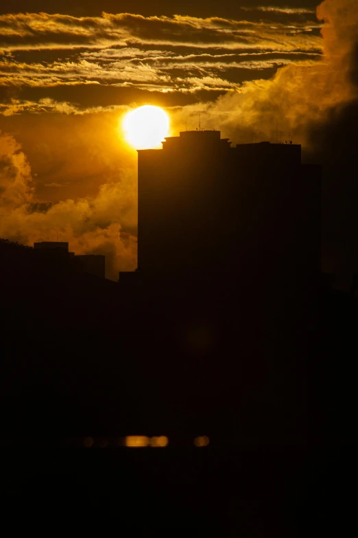 the sun rises behind tall buildings on a cloudy evening