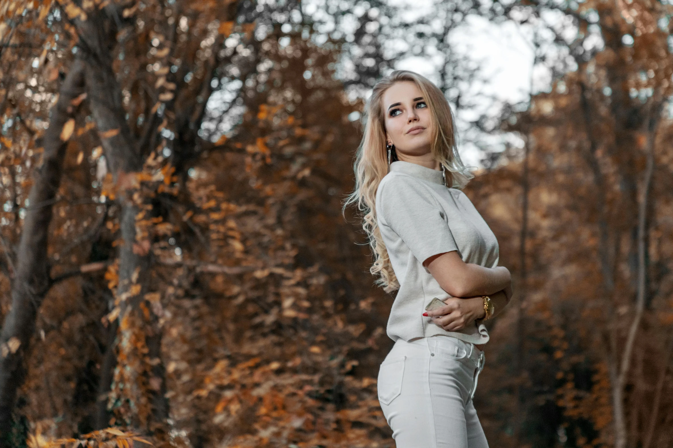 a woman standing in a wooded area with her arms crossed