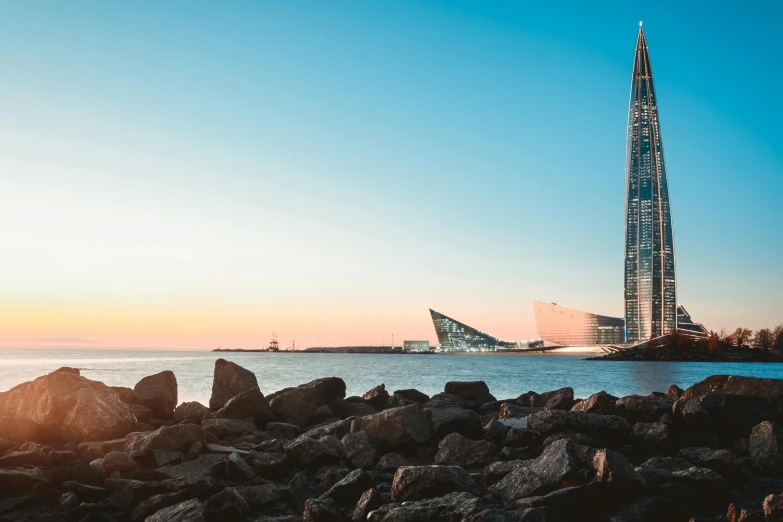 a modern skyscr and a rocky shoreline with the sun setting