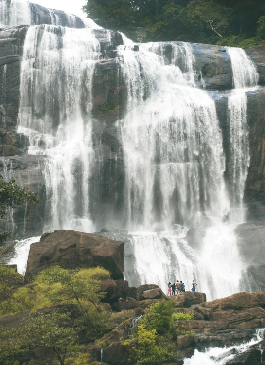 several people stand on the rocks looking out at waterfall