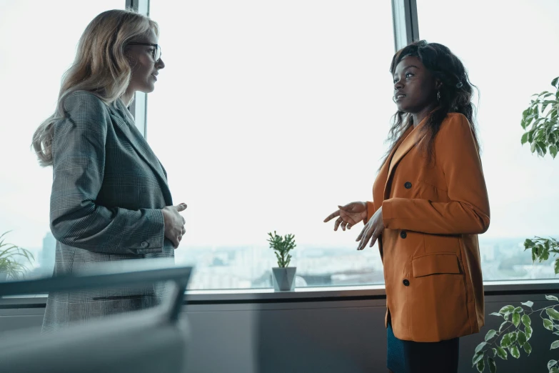 two women talking in a room near large windows