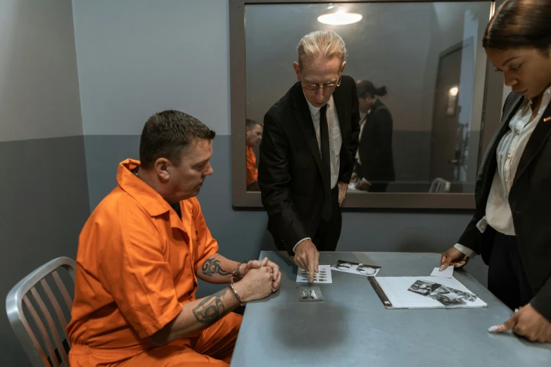 a man sitting at a table in an orange prison uniform looking at pictures