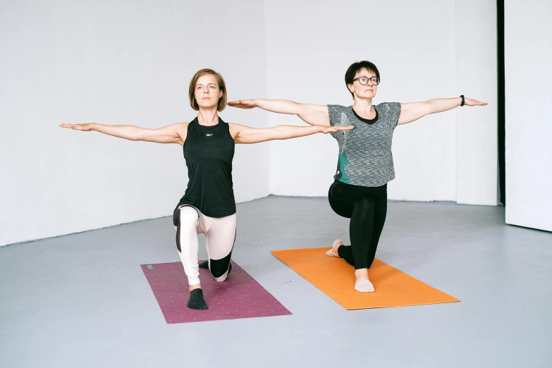 two women on yoga mats doing stretches in an empty room