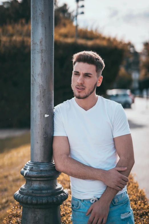 a young man leaning on a pole in a white shirt