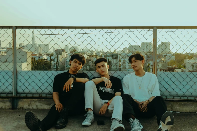 three boys sit near a fence and look at the camera