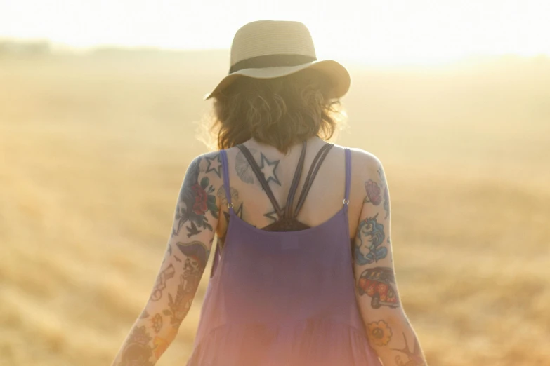tattooed woman with hat in open grassy field