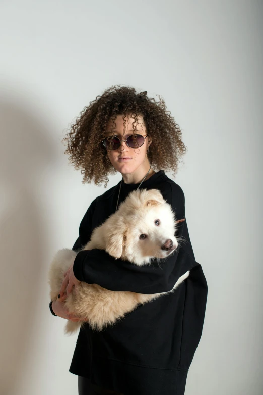 a woman holding two dogs while standing in front of a white wall