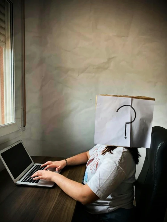 woman sitting in an office with the head of a paper bag over her head that says f on it