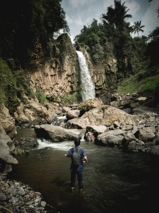 two people standing in a shallow river near a waterfall