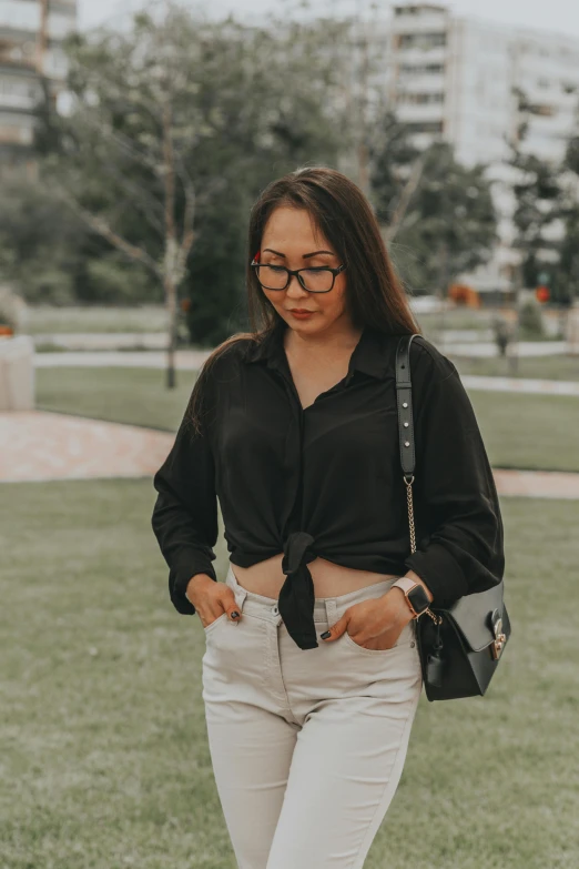 a woman with glasses is holding her cell phone and standing on grass