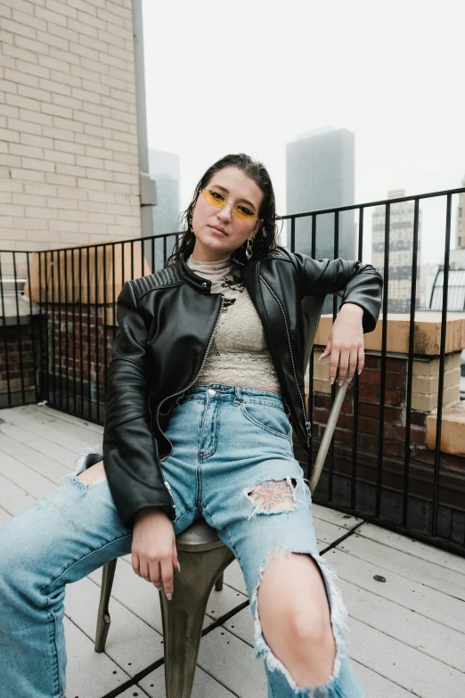 a woman in ripped jeans and leather jacket sits on a chair