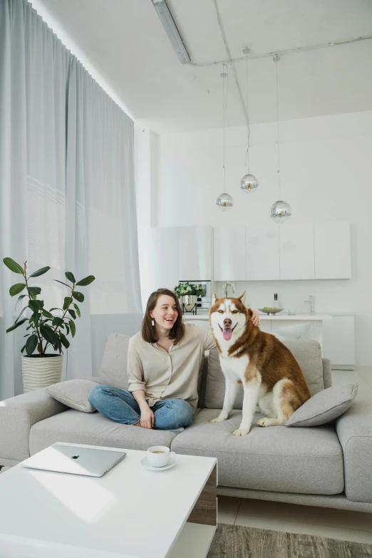 a woman sits on a couch next to her dog