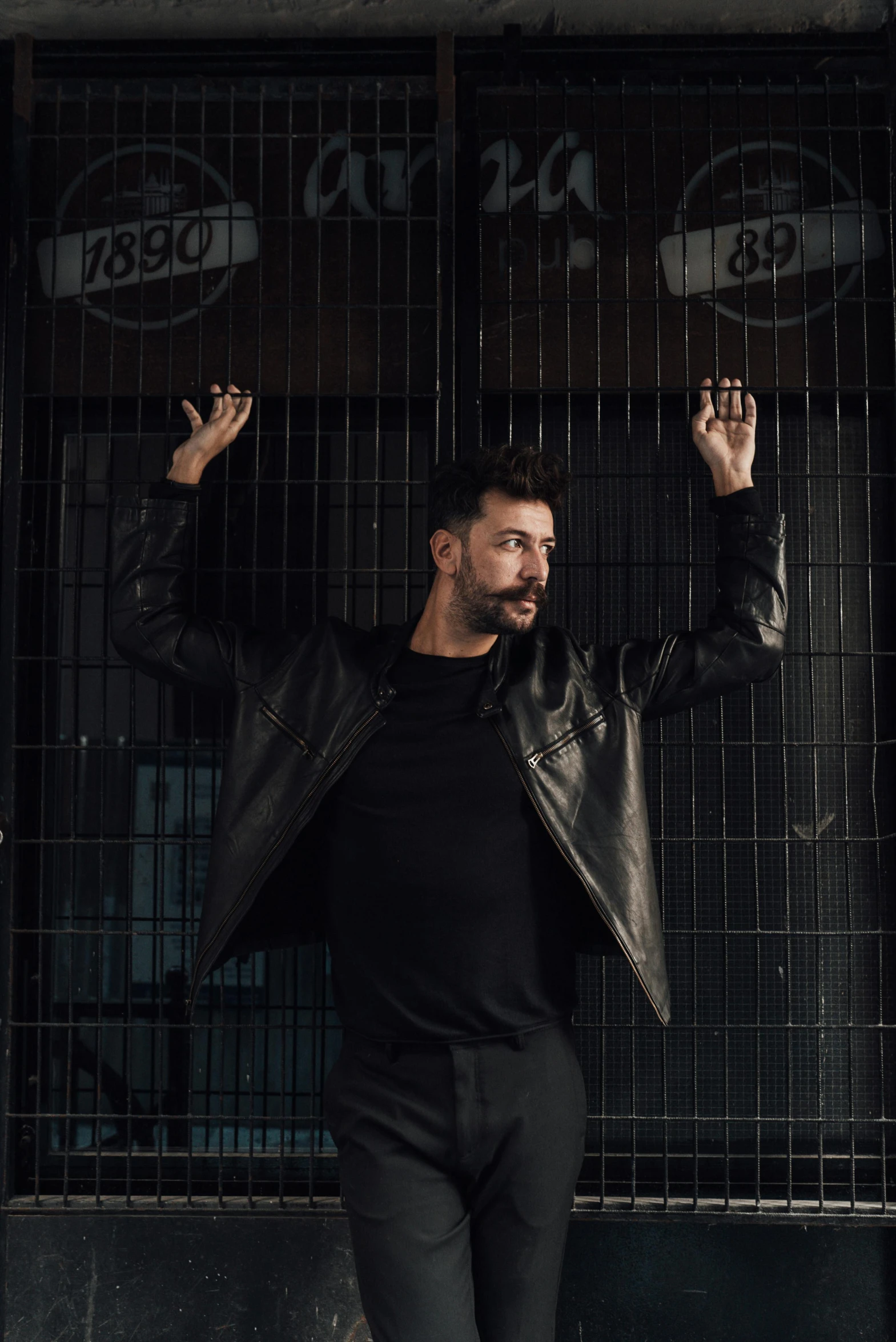 a man standing in front of metal fences, arms raised and wearing black