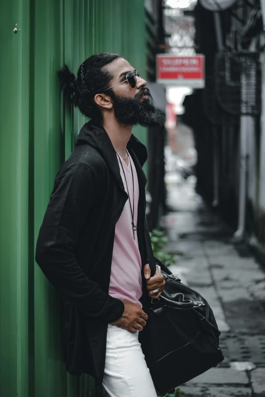 a man leaning on a green wall, holding his bag