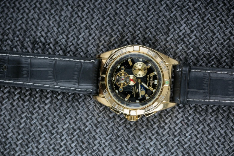 a black watch with gold accents is lying on some fabric