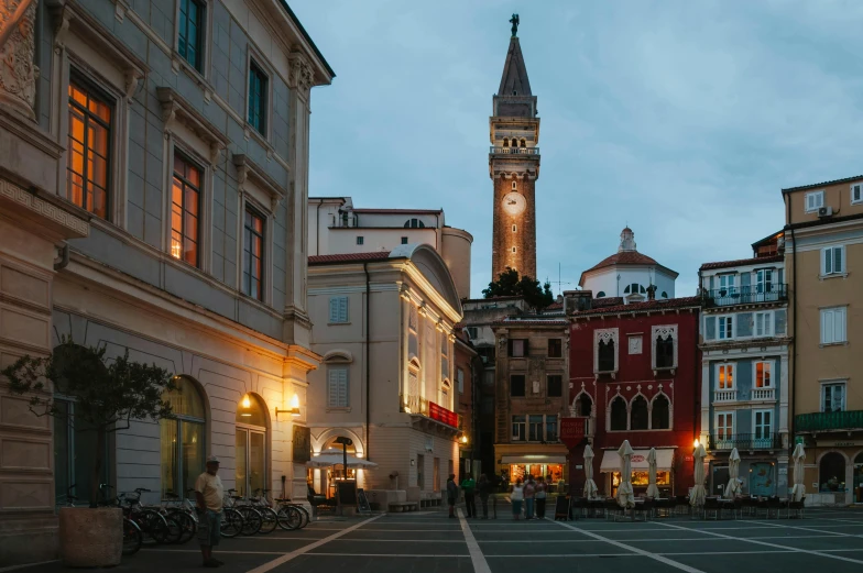 a street with buildings and an old clock tower lit up at dusk