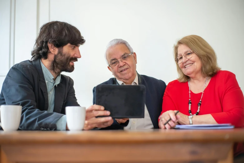 three people sitting around a table in an office looking at soing on a tablet