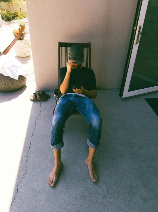 a man that is sitting in the shade with his cell phone