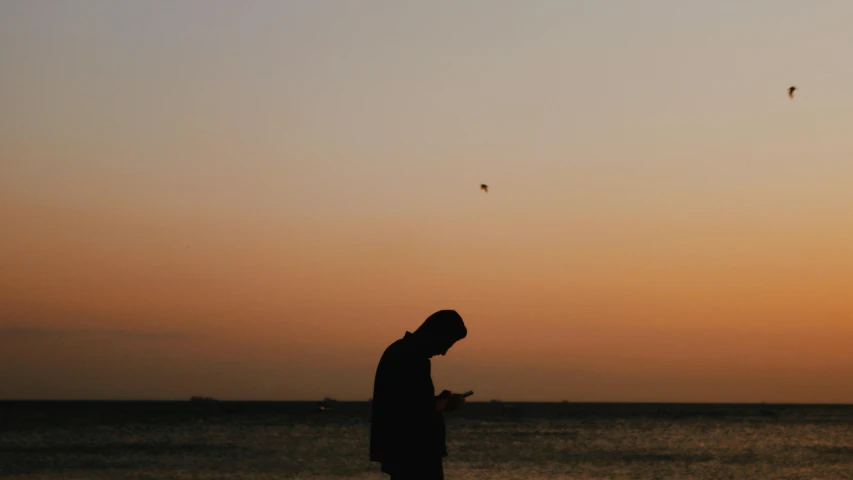 a person in silhouette standing on the beach at sunset
