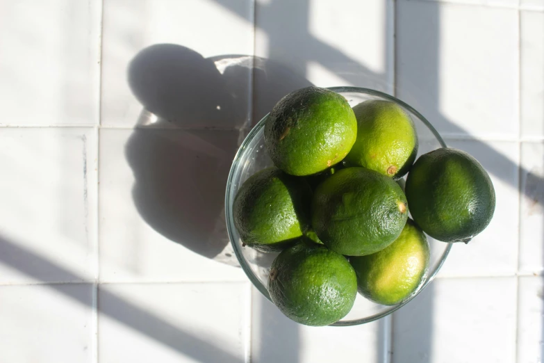 some limes in a glass bowl on a tiled table