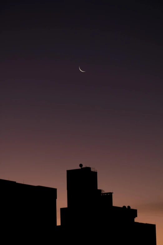 the sky at dusk over a building under a crescent