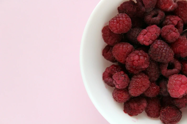 a bowl filled with raspberries on top of a pink table