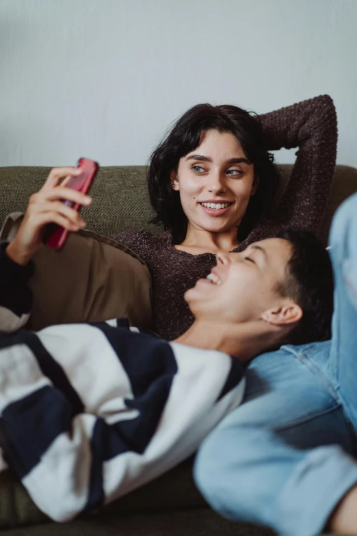 two people lying on top of a couch while looking at a cellphone