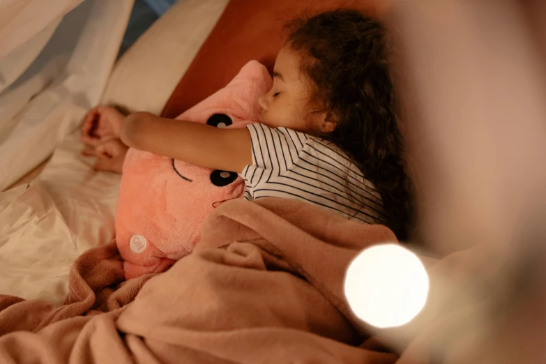 a little girl in bed with a pink stuffed animal