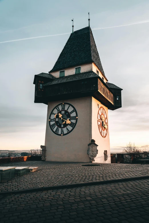 the clock tower on the cobblestone street is illuminated by evening sun