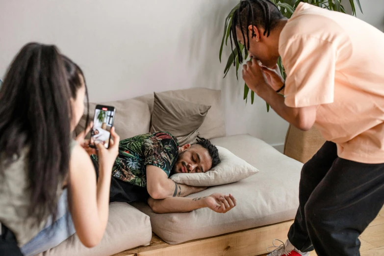 two people stand by a sofa, the person is laying on a pillow