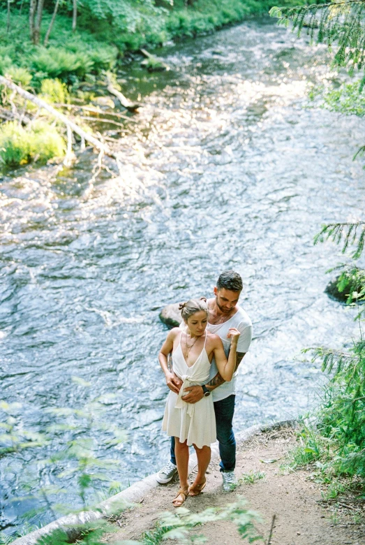 a young man carrying a small girl as he stands in front of a creek