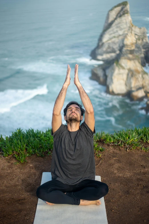 a man sits on his feet doing yoga in front of a large rock cliff