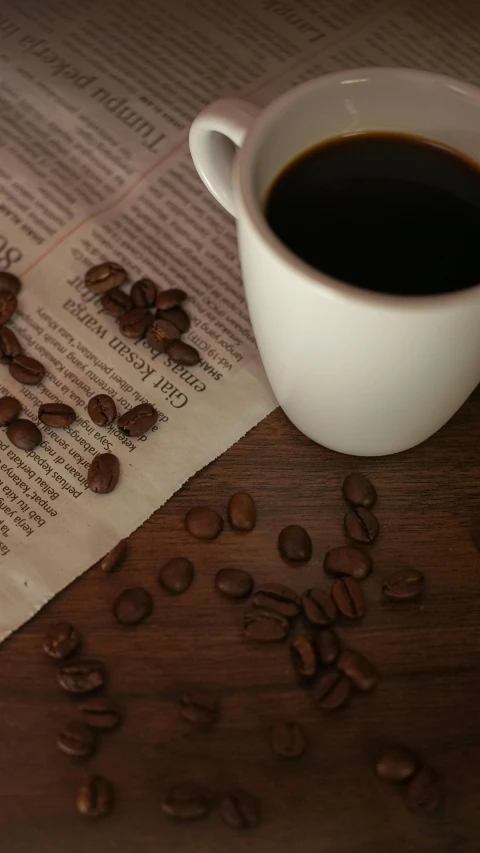 a cup of coffee next to a newspaper with roasted beans
