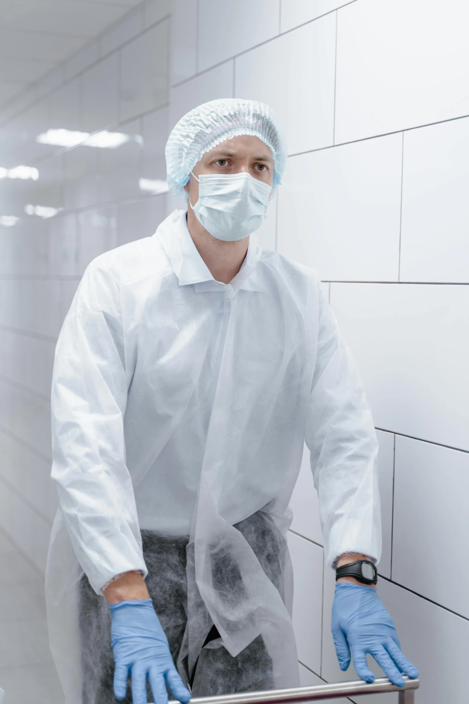 a man in surgical clothing, gloves and medical mask is leaning against a wall