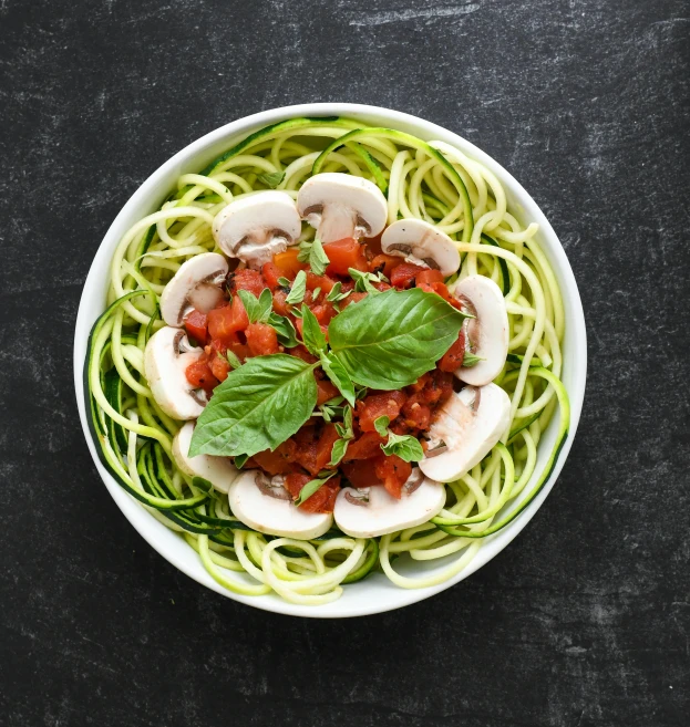 a pasta dish has mushrooms, tomato, and green pesto