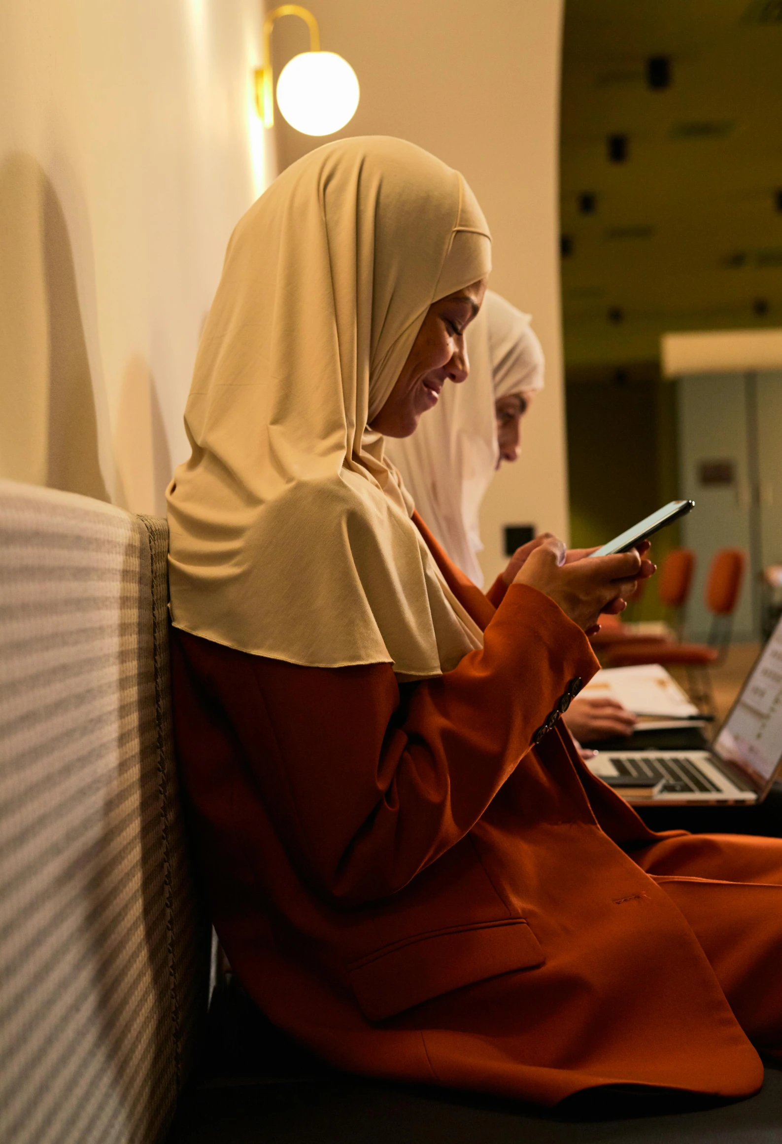 women sit side by side, one using a cell phone