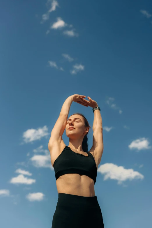 a woman is standing under a blue sky and stretching her arms to the sky