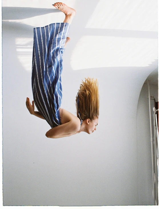 a man in a blue striped shirt and jeans is upside down