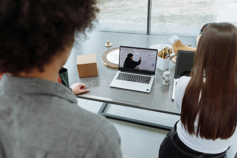 two people sit at a desk with an open laptop