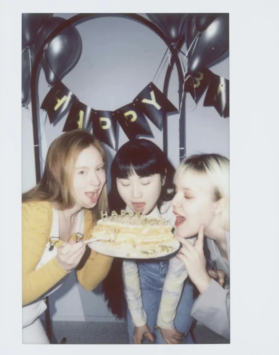 three women pose with a cake in front of a party sign