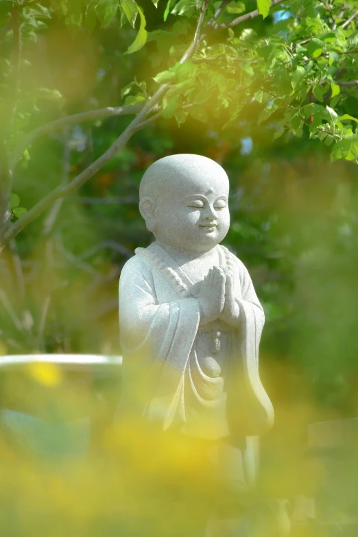 a white buddha statue standing next to a bush
