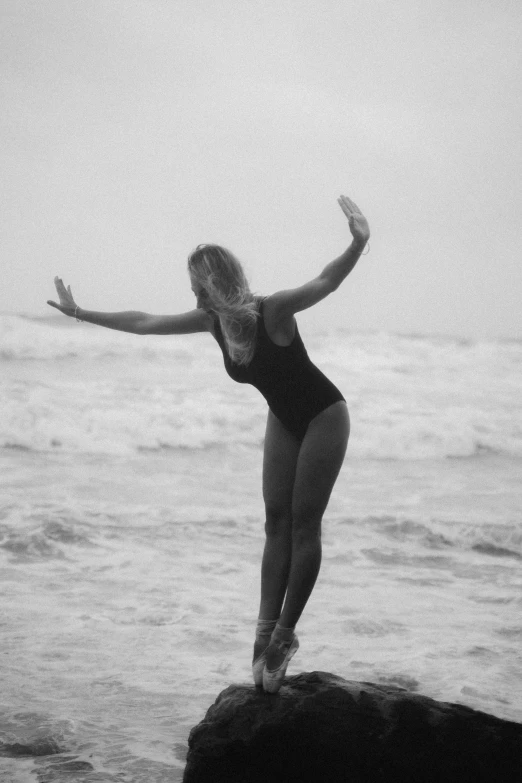 a woman standing on top of a rock near the ocean