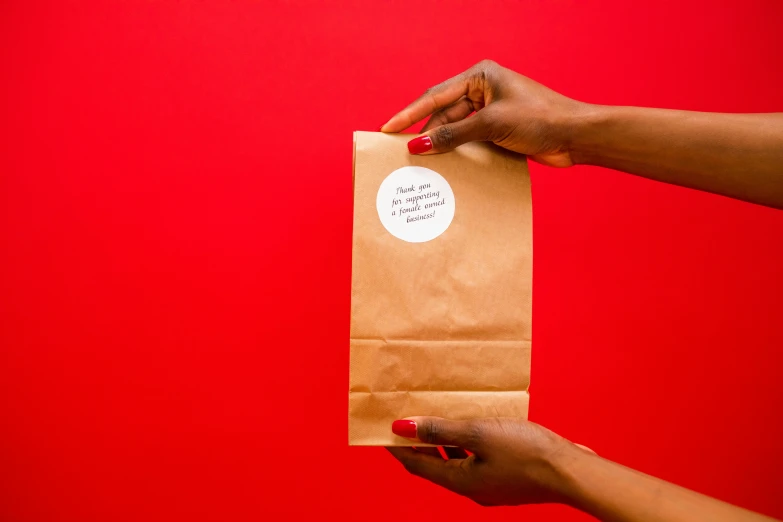 two hands holding a brown paper bag with sticker on it