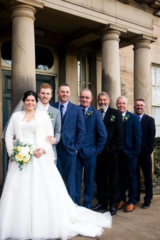 a group po of a bride and groom posing for a wedding picture with friends in front of the building